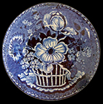 Pearlware saucer reverse printed underglaze in dark blue. Field dots decorative device forms background behind flowers.  Impressed Clews mark and triangle on reverse. James and Ralph Clews (1814-1834), Cobridge.  Transferware Collectors Club names this pattern Basket. 5.5” rim diameter, 1.0” vessel height.